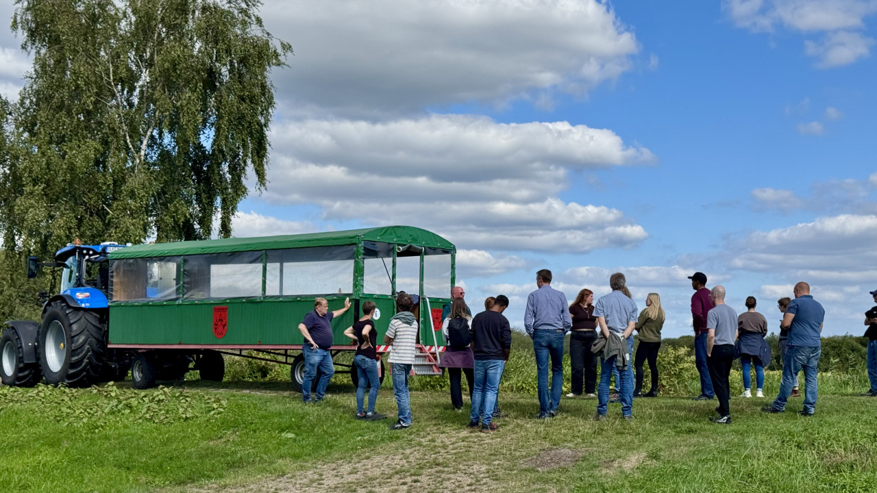 Personengruppe vor einem Traktor mit Planwagen, umgeben von grüner Natur.