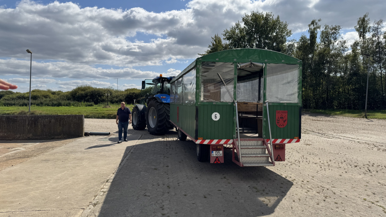 Ein Trecker mit Planwagen, davor steht eine Person.