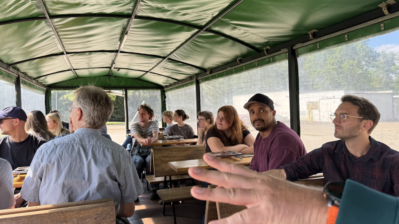 Personen im Planwagen schauen aus den Fenstern, während eine Hand nach links zeigt.